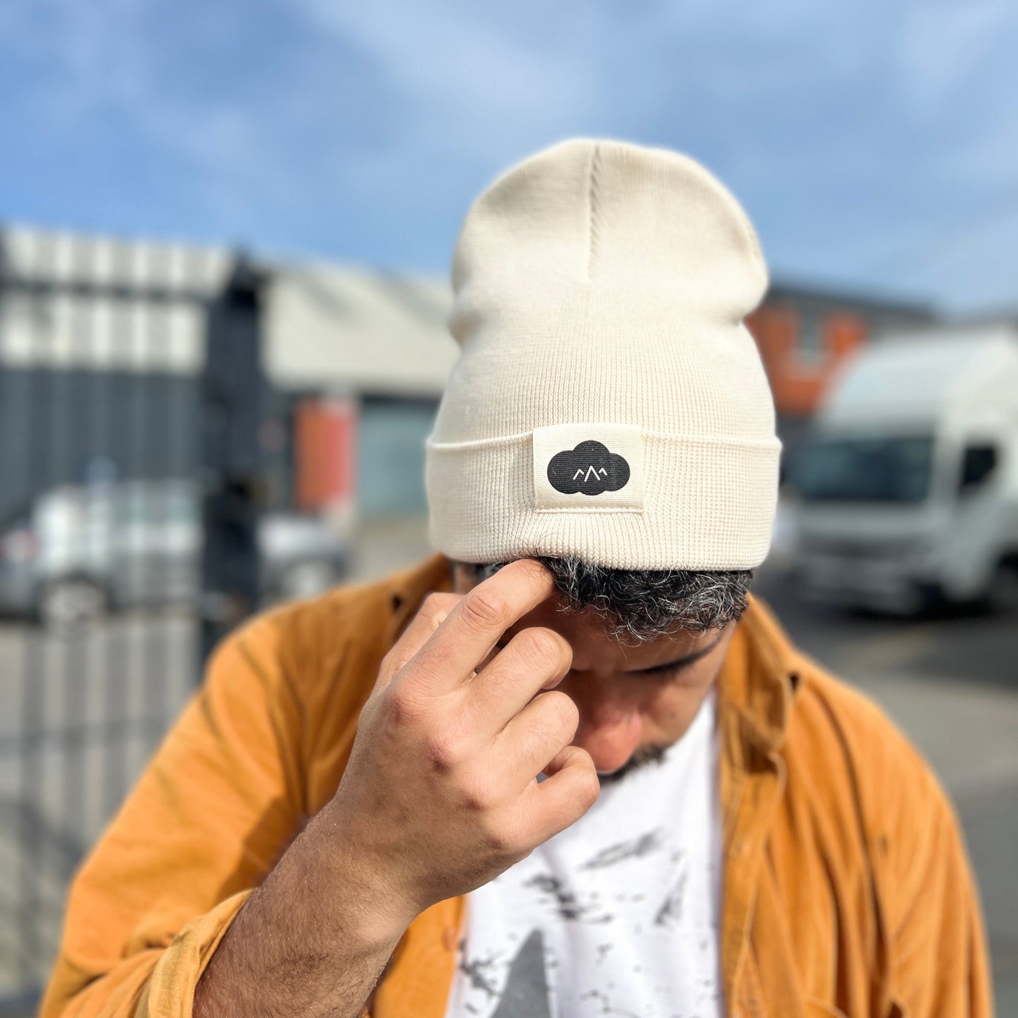 Person wearing a beige beanie with a logo, covering their face outdoors.